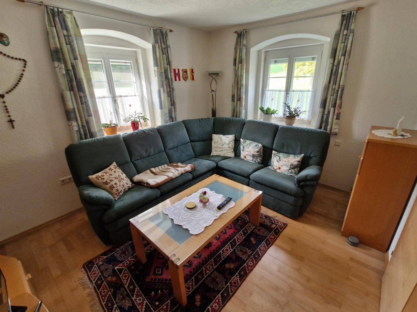 Helles Wohnzimmer mit bequemer Sitzecke, Holzboden und zwei Fenstern für viel Tageslicht.