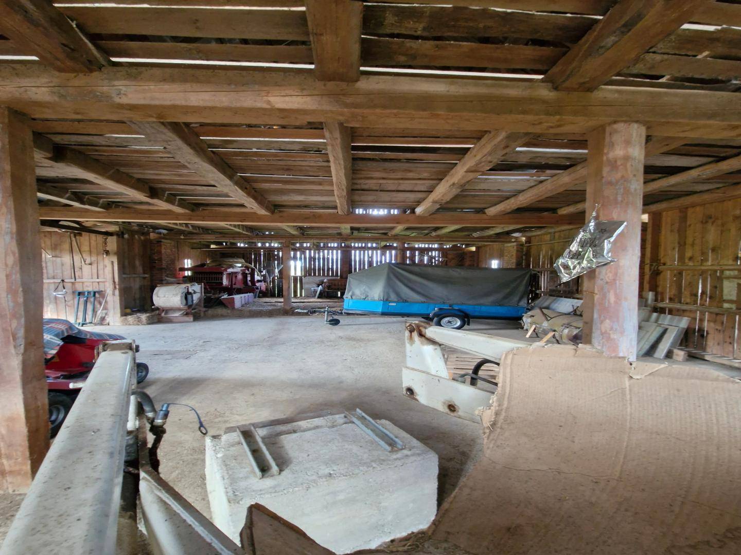 Geräumige Scheune mit sichtbaren Holzbalken, Betonboden und verschiedenen Geräten, bietet viel Nutzfläche.