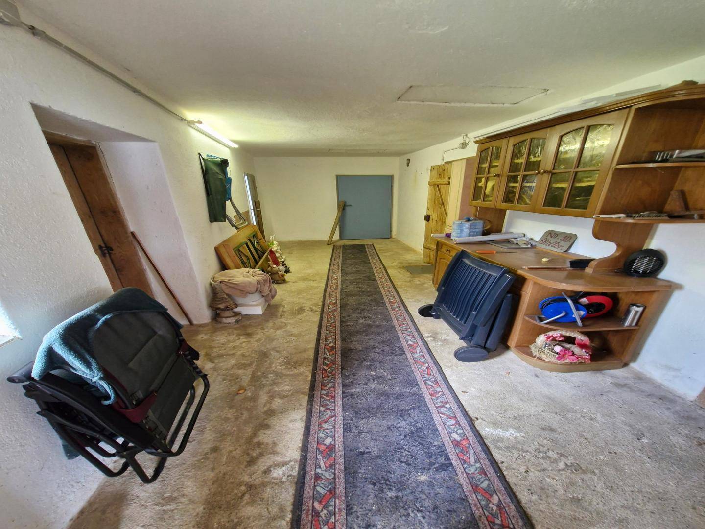 Geräumiger Lagerraum oder Werkstatt mit Betonboden, einem langen Teppich und Holzschränken, vielseitig nutzbar.