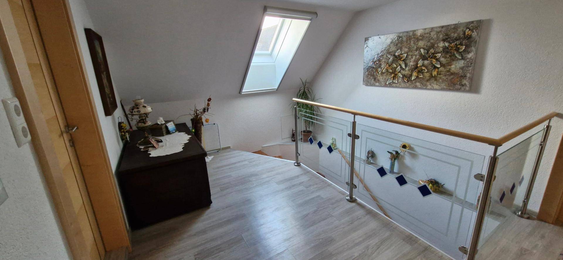 Heller Treppenabsatz im Obergeschoss mit Dachfenster und modernem Glasgeländer.