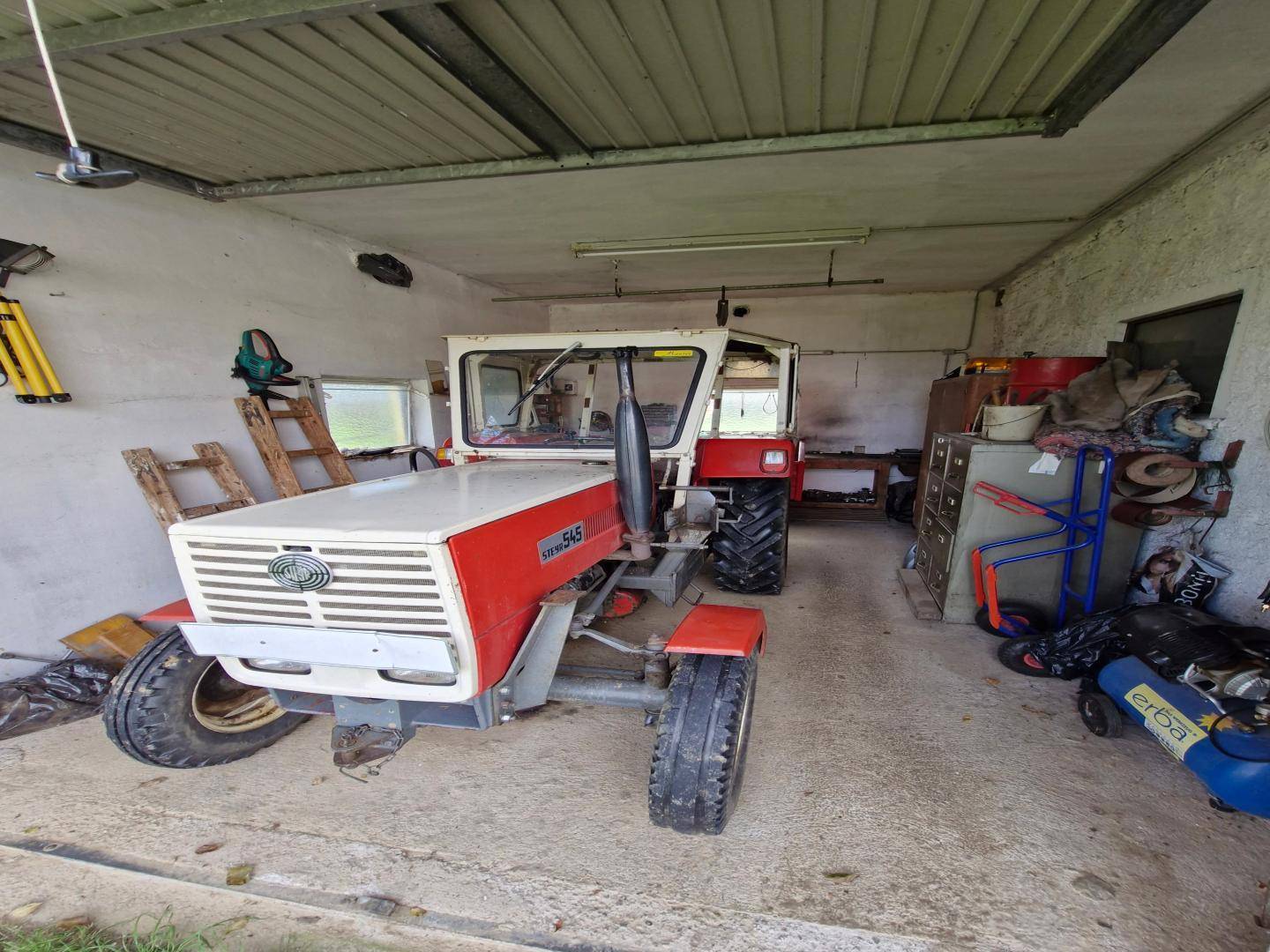Geräumige Garage oder Scheune mit einem Traktor, Werkzeugen und verschiedenen Geräten, ideal für Lagerung.