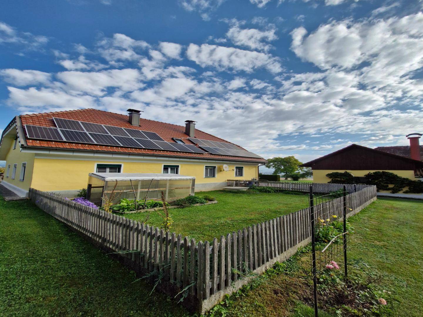Seitenansicht des Hauses mit Solarpaneelen auf dem Dach und einem kleinen, eingezäunten Gartenbereich.