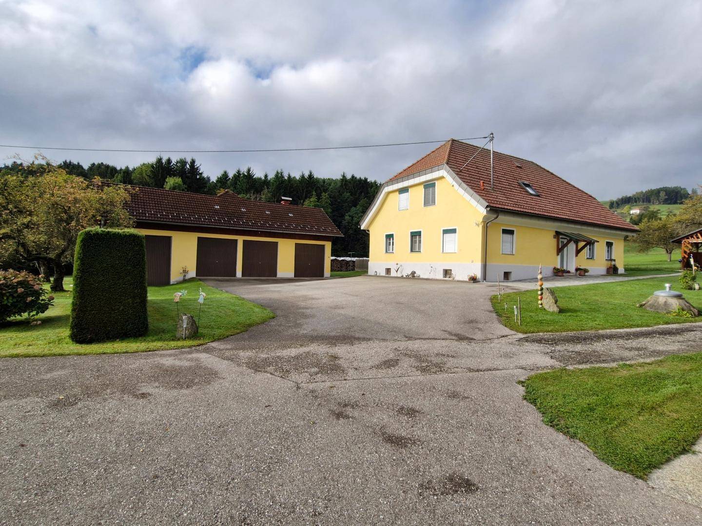 Gelbes Wohnhaus und separates Garagengebäude mit Zufahrt und gepflegtem Rasen, umgeben von Natur.