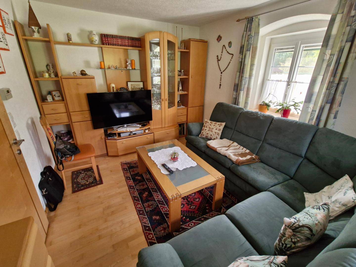 Gemütliches Wohnzimmer mit großem Ecksofa, Holzmöbeln und Blick ins Grüne durch die Fenster.
