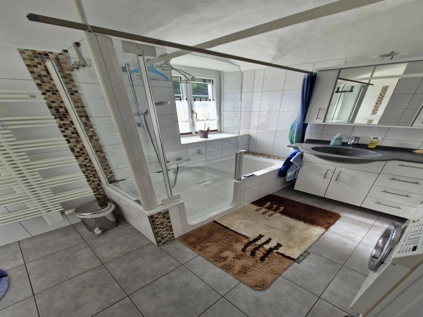 Modernes Badezimmer mit Waschtisch, begehbarer Dusche und Waschmaschine, hell gefliest.