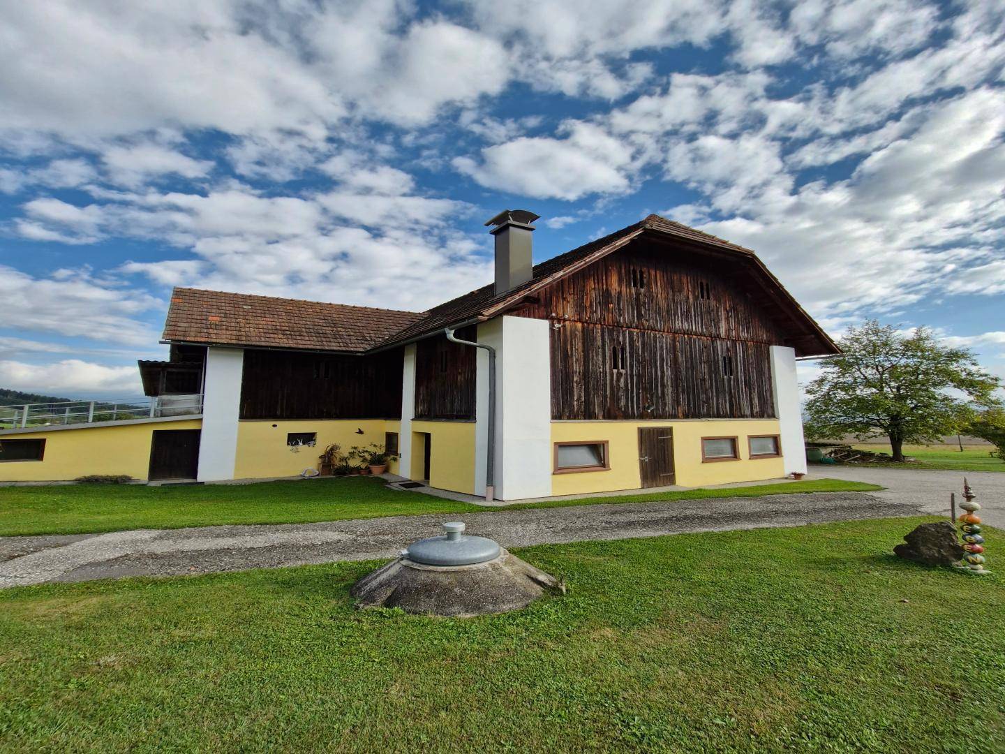 Traditionelles Gebäude mit gelber Fassade und dunkler Holzverkleidung, umgeben von einer weitläufigen Rasenfläche.