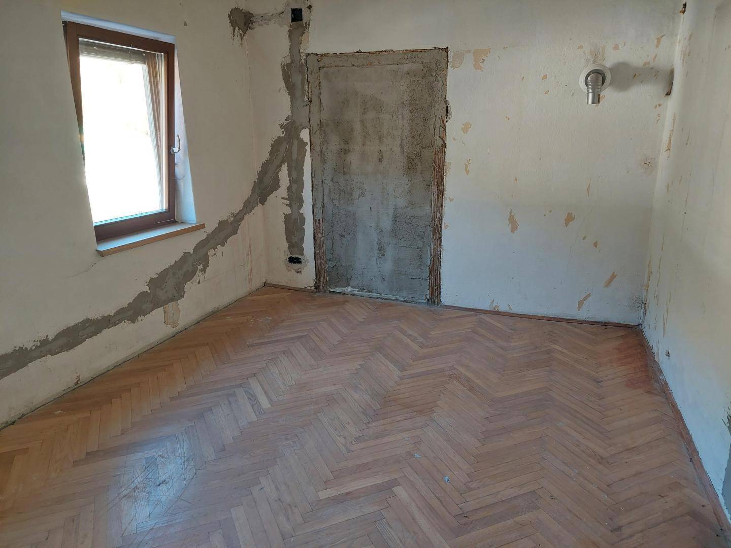 Leerer Raum im Renovierungszustand mit Fischgrätparkett und einem Fenster.