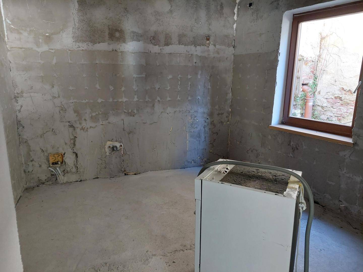 Rohbauküche mit vorbereiteten Anschlüssen und einem Fenster, bereit für den Einbau.