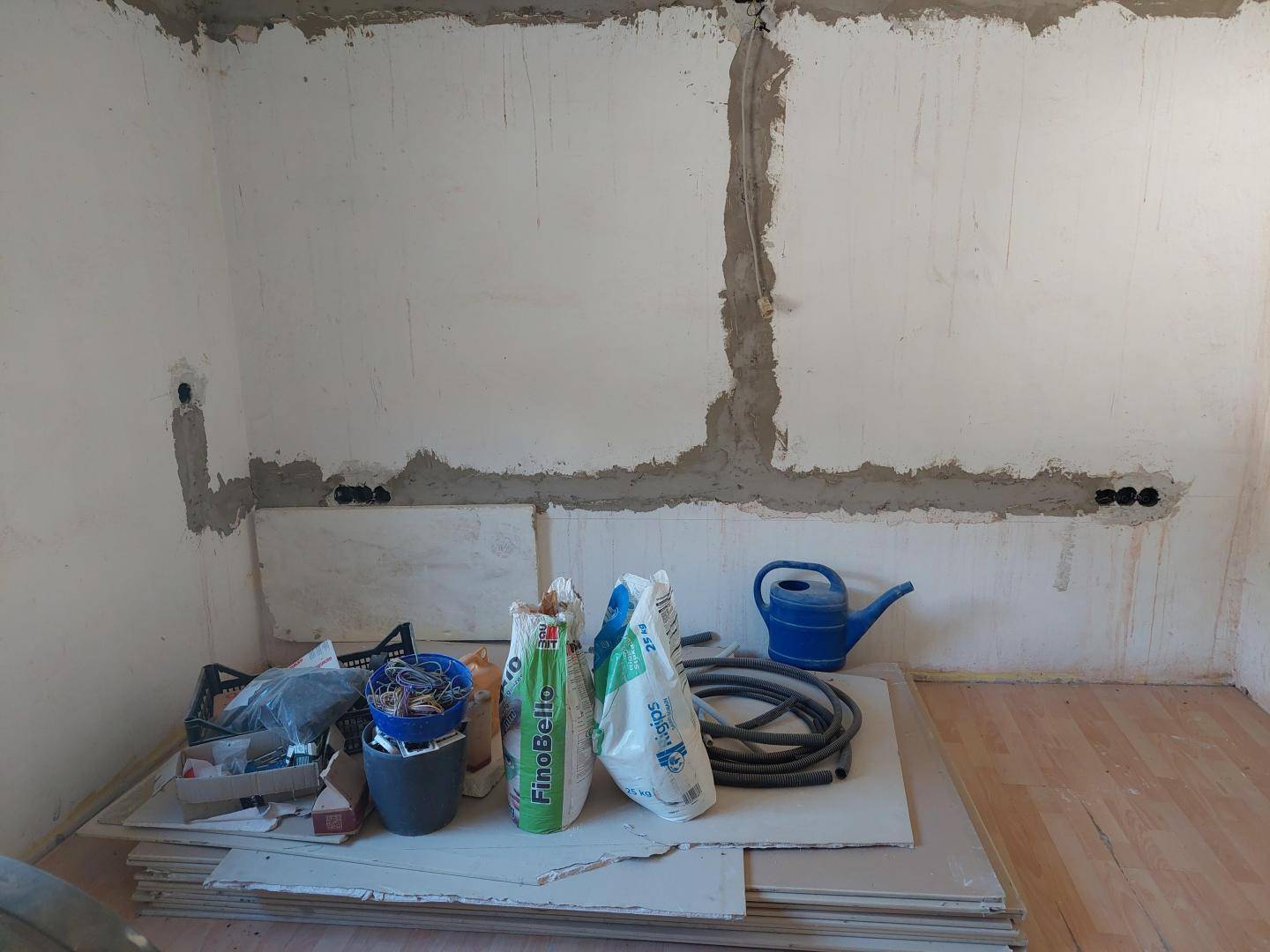 Innenraum im Rohbau mit Baumaterialien und vorbereiteten Elektroinstallationen.