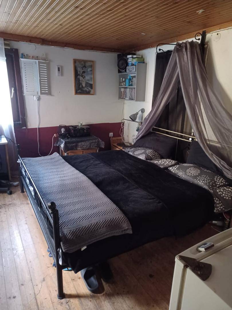 Schlafzimmer mit Holzbalkendecke, Doppelbett und einfacher Einrichtung, beleuchtet durch ein Fenster.
