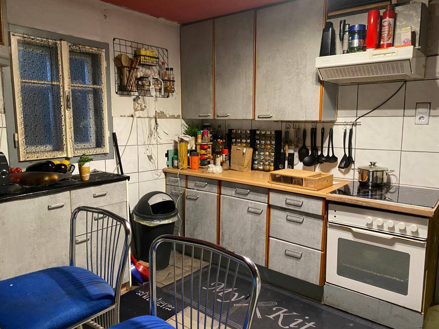 Funktionale Küche mit grauen Schränken, Holztheke und einem Elektroherd mit Kochfeld.