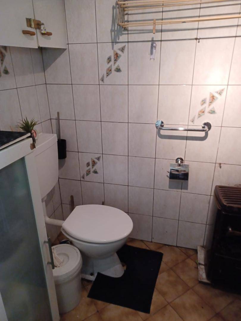 Separate Toilette mit weißen Fliesen, einem WC und einem kleinen Heizkörper, einfach eingerichtet.