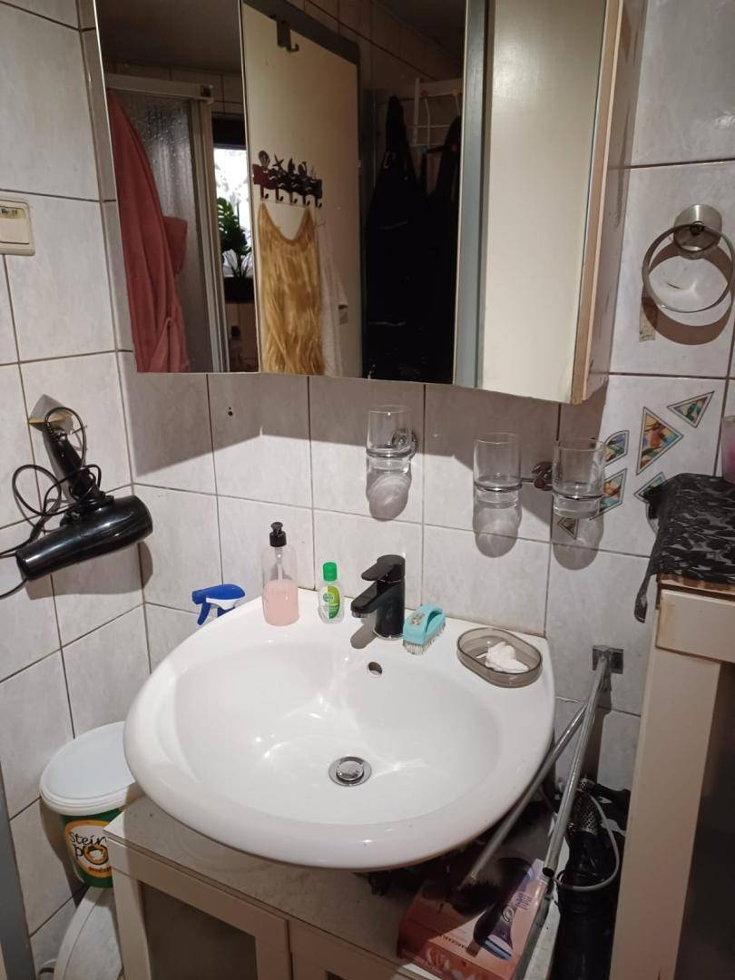 Kleines Badezimmer mit Waschbecken, Spiegel und weißen Fliesen, ausgestattet mit einem Medizinschrank.