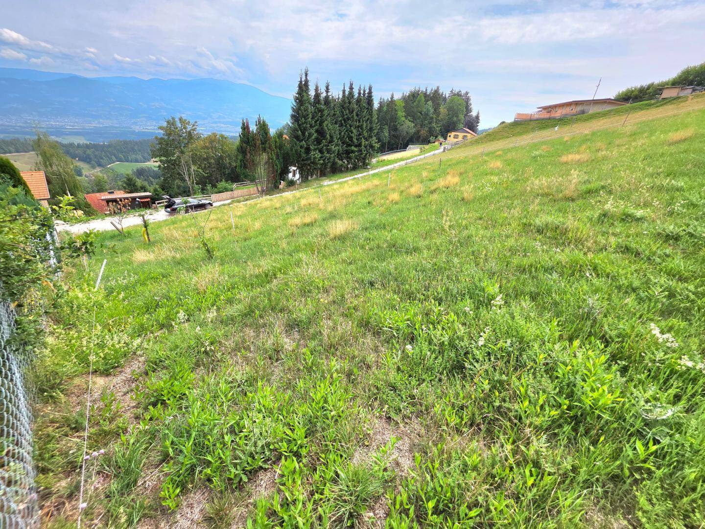 Grünes Hanggrundstück mit Blick auf die umliegende Landschaft und entfernte Berge unter weitem Himmel.
