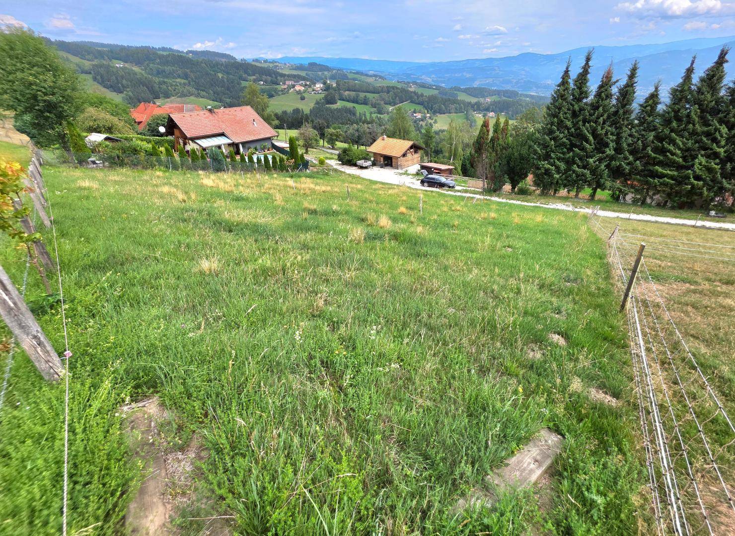 Weitläufiges grünes Grundstück mit Blick auf mehrere Häuser und die hügelige Landschaft in der Ferne.