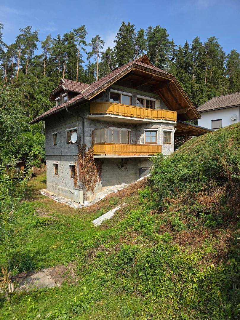 Rückansicht des Hauses mit mehreren Balkonen, umgeben von dichtem Wald und viel Grün.