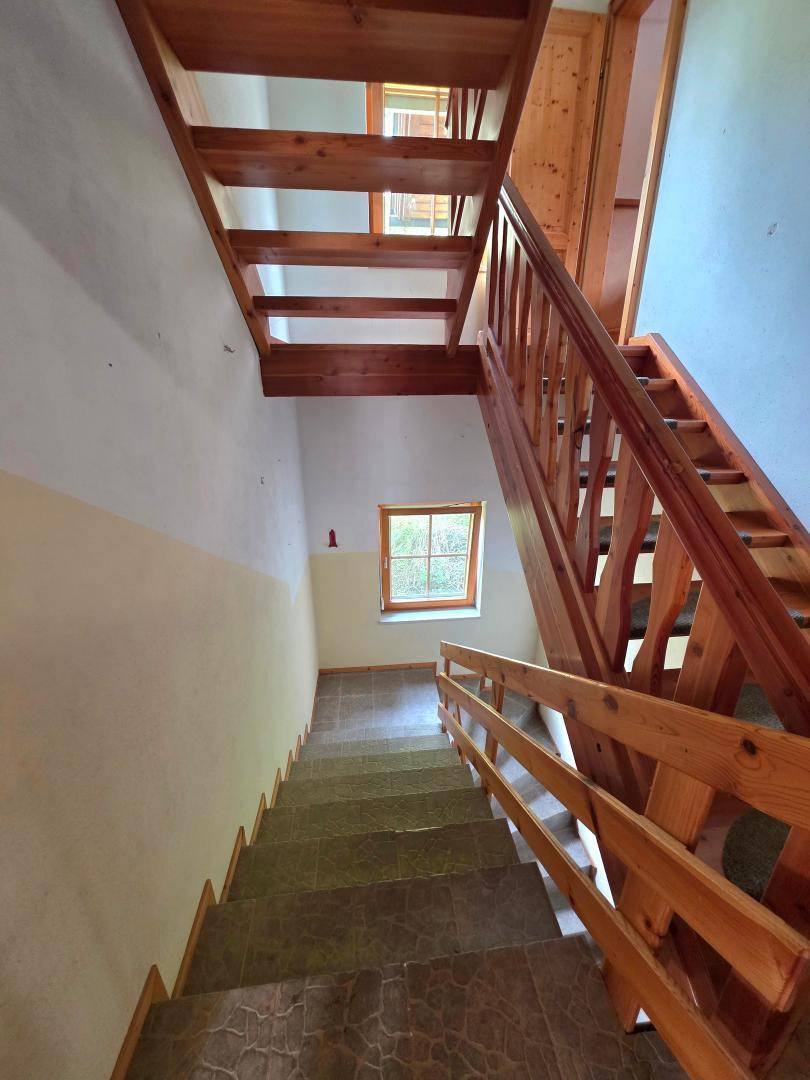 Treppenhaus mit Holztreppe und Fliesenboden, das die verschiedenen Etagen verbindet.