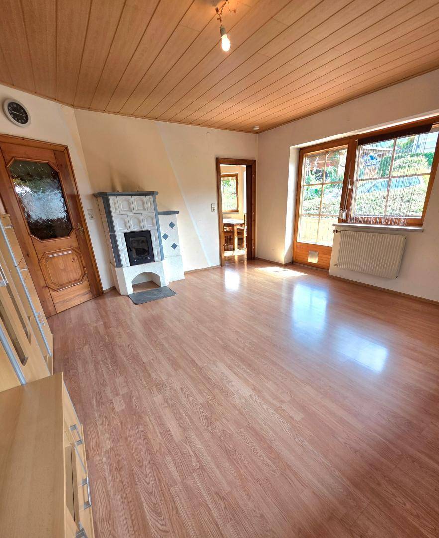 Gemütliches Wohnzimmer mit Laminatboden, Kachelofen und Zugang zu einem Balkon.