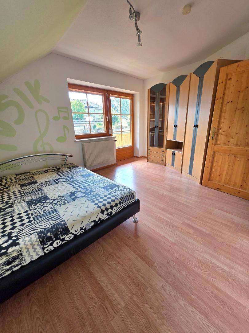 Schlafzimmer mit Laminatboden, Bett und Kleiderschrank, mit Zugang zu einem Balkon.
