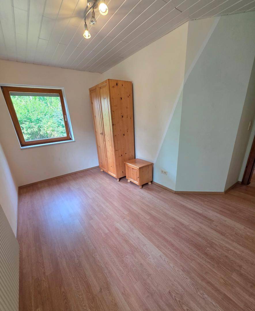 Schlafzimmer mit Laminatboden, Holzschrank und Dachschräge, bietet eine gemütliche Atmosphäre.