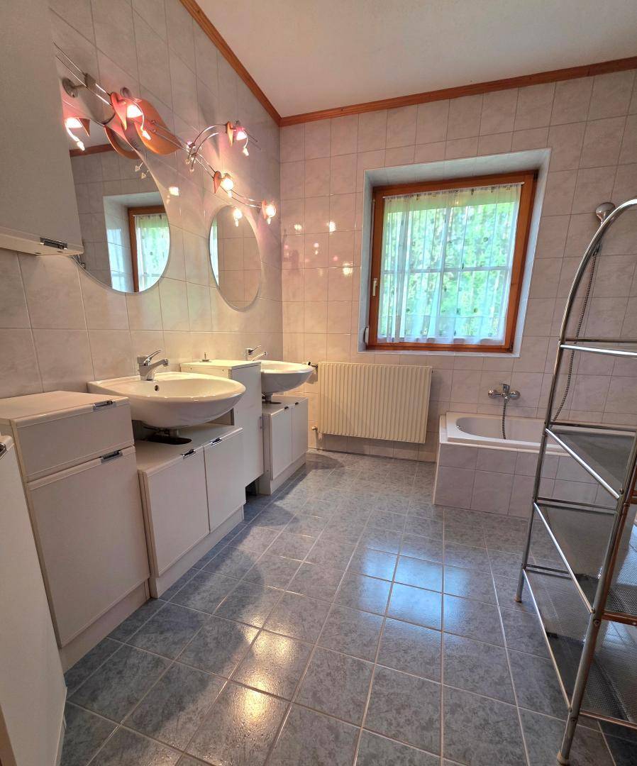 Geräumiges Badezimmer mit Doppelwaschbecken, Badewanne und Fenster, in hellem Design.