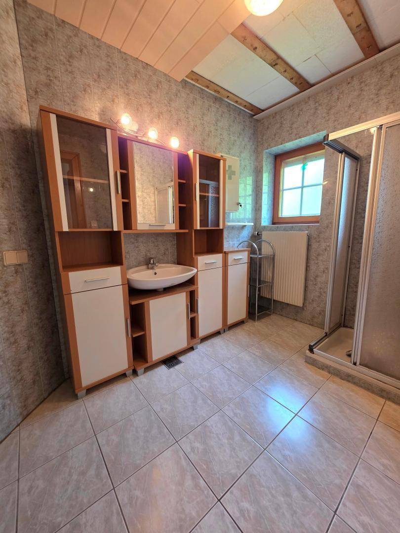 Badezimmer mit Fliesenboden, Duschkabine und großem Waschtischunterschrank mit Spiegel.