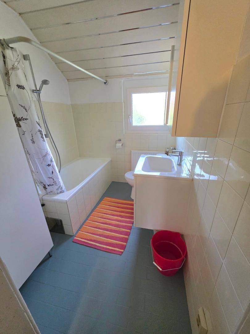 Funktionales Badezimmer mit Badewanne, Duschvorhang, Waschbecken und Fenster für Tageslicht.