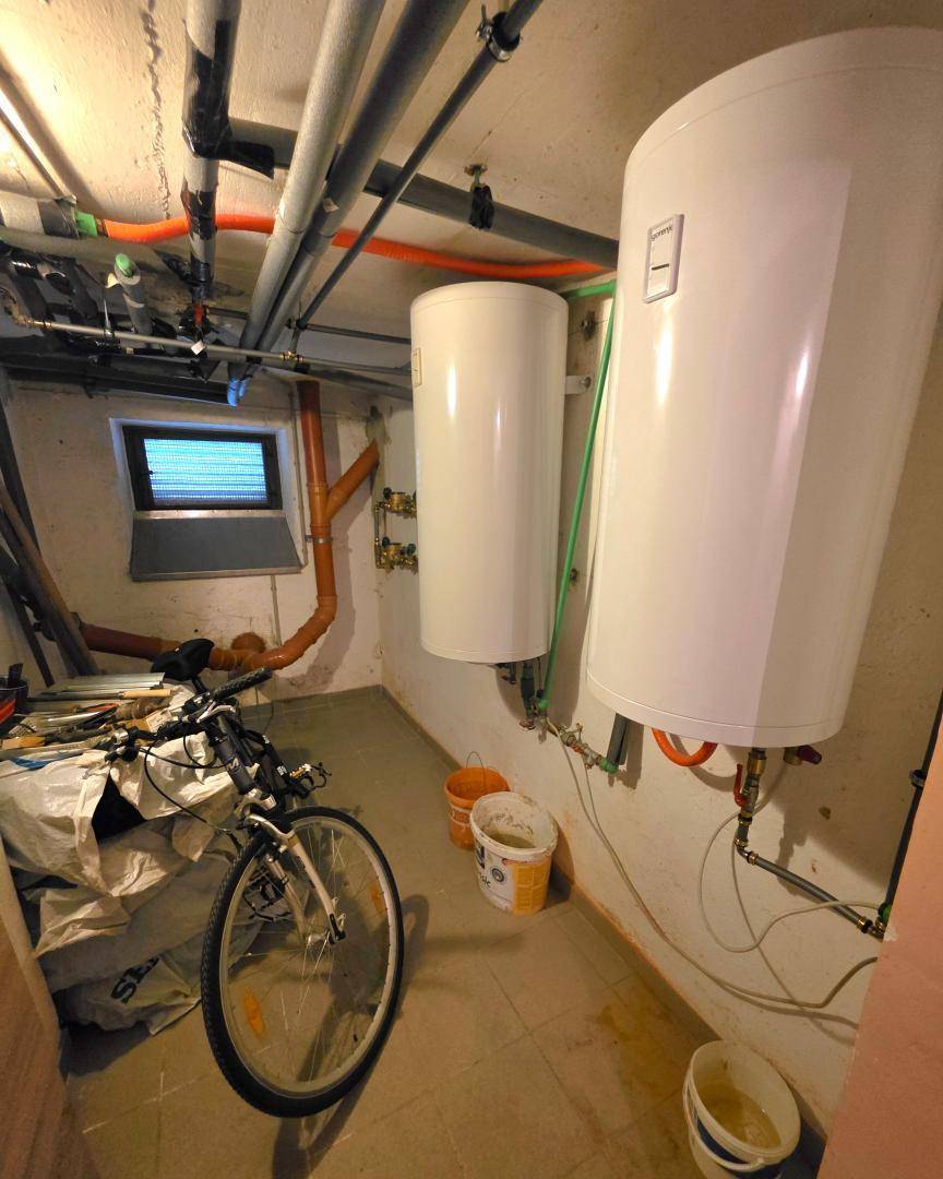 Heizungsraum im Keller mit Warmwasserspeichern und sichtbaren Rohrleitungen, funktional und aufgeräumt.