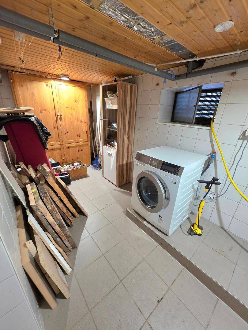 Waschküche im Keller mit Waschmaschine, gefliestem Boden und Holzdecke, praktisch eingerichtet.