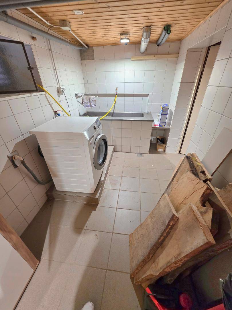 Kellerraum mit Waschmaschine, großem Waschbecken und gefliesten Wänden, dient als Hauswirtschaftsraum.