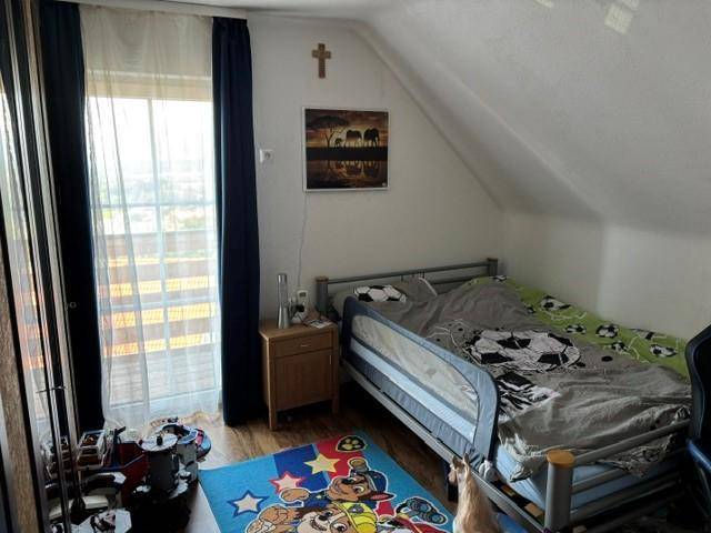 Kinderzimmer mit Einzelbett, Nachttisch und Zugang zu einem Balkon unter der Dachschräge.