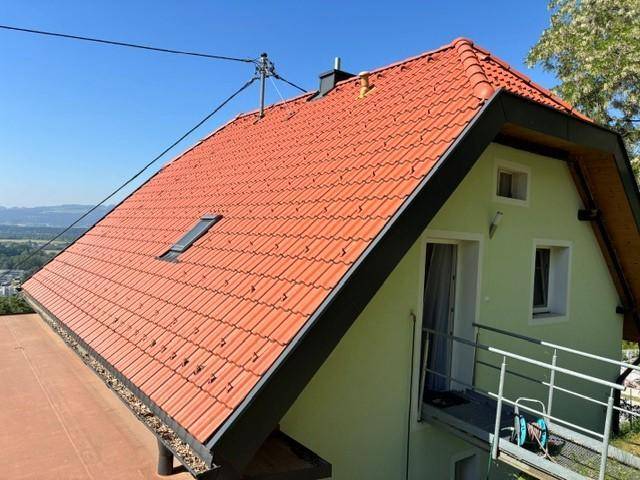 Seitenansicht des Hauses mit rotem Ziegeldach, hellgrüner Fassade und kleinem Balkonzugang.