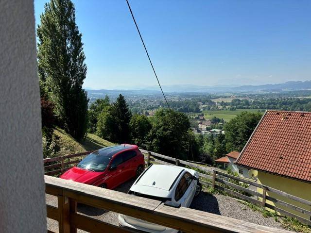 Blick vom Balkon auf geparkte Autos und die weite, grüne Landschaft im Hintergrund.
