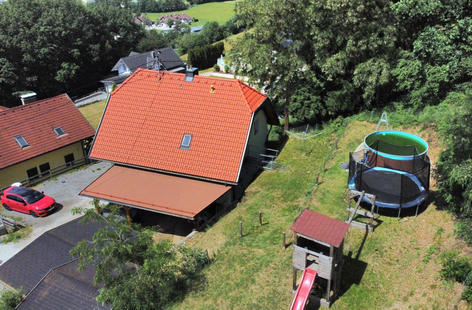 Überblick über den hinteren Bereich des Hauses mit Pool, Trampolin und Spielturm im grünen Garten.