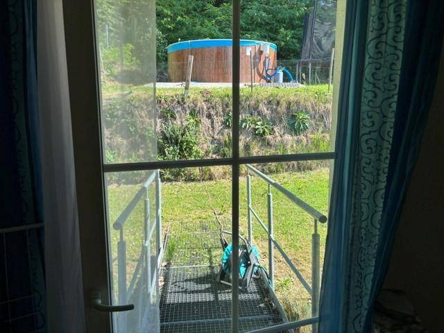 Blick aus dem Innenraum durch eine Tür auf eine Metalltreppe, die zum Garten mit Pool führt.