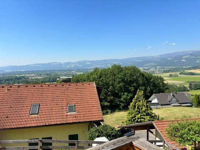 Weitblick über Dächer und grüne Landschaft bis zu den fernen Bergen unter blauem Himmel.