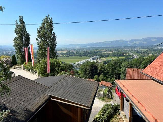 Panoramablick von oben über Dächer, Bäume und ein weites Tal mit Fernsicht.