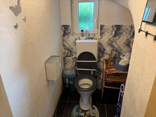 Kleines WC mit Toilette, Fenster und einer Wandgestaltung in Marmoroptik.