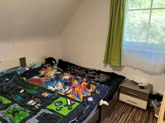 Kinderzimmer mit Bett, Nachttisch und Fenster, unter einer gemütlichen Dachschräge gelegen.