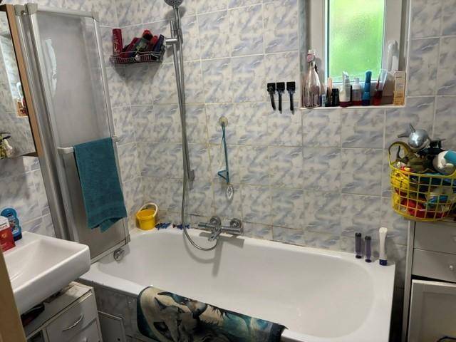Badezimmer mit Badewanne, Duschvorrichtung, Waschbecken und hellblau gemusterten Fliesen.