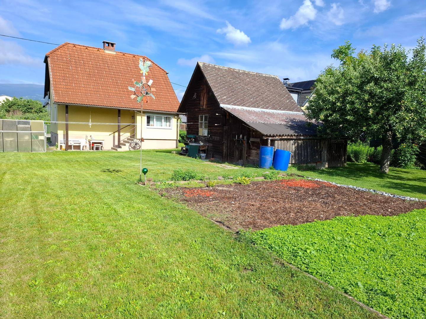 Großer grüner Garten mit Rasenfläche, Anbaufläche und einem rustikalen Nebengebäude.