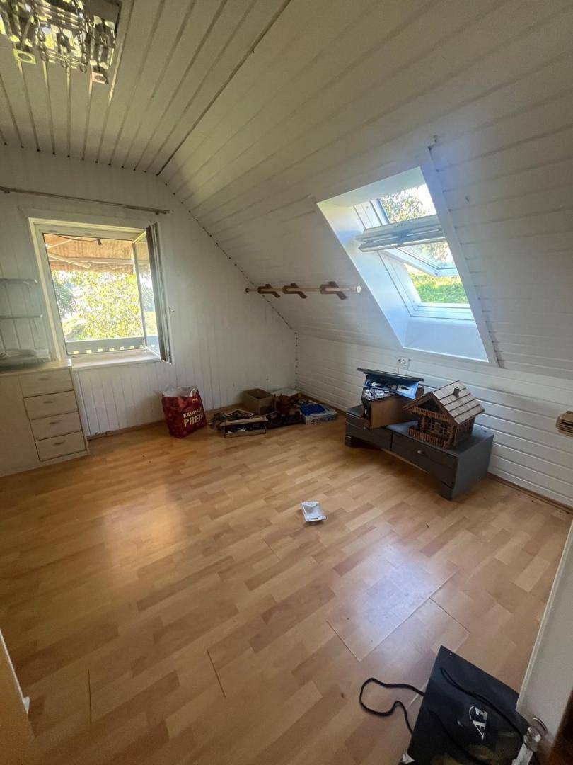 Helles Dachgeschosszimmer mit schrägen Wänden, Dachfenstern und Blick ins Grüne.