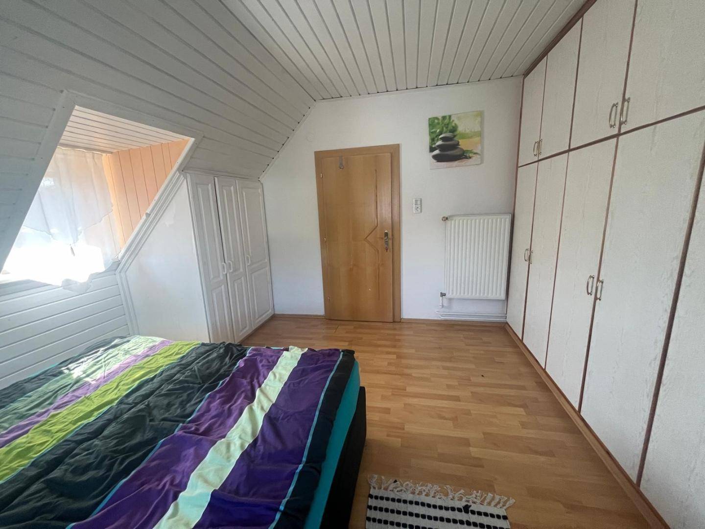 Schlafzimmer im Dachgeschoss mit schrägen Wänden, Einbauschränken und hellem Laminatboden.