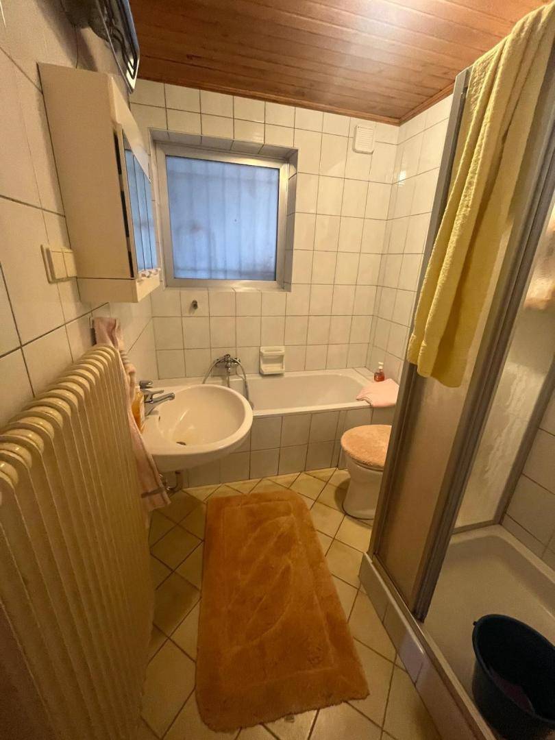 Kleines Badezimmer mit Badewanne, Dusche, Waschbecken und Fliesen im 80er-Jahre-Stil.