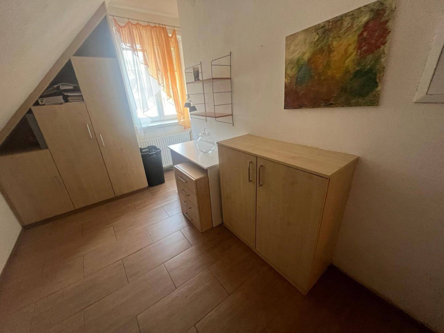 Kleines Arbeitszimmer im Dachgeschoss mit Schreibtisch, Schränken und schrägen Wänden.
