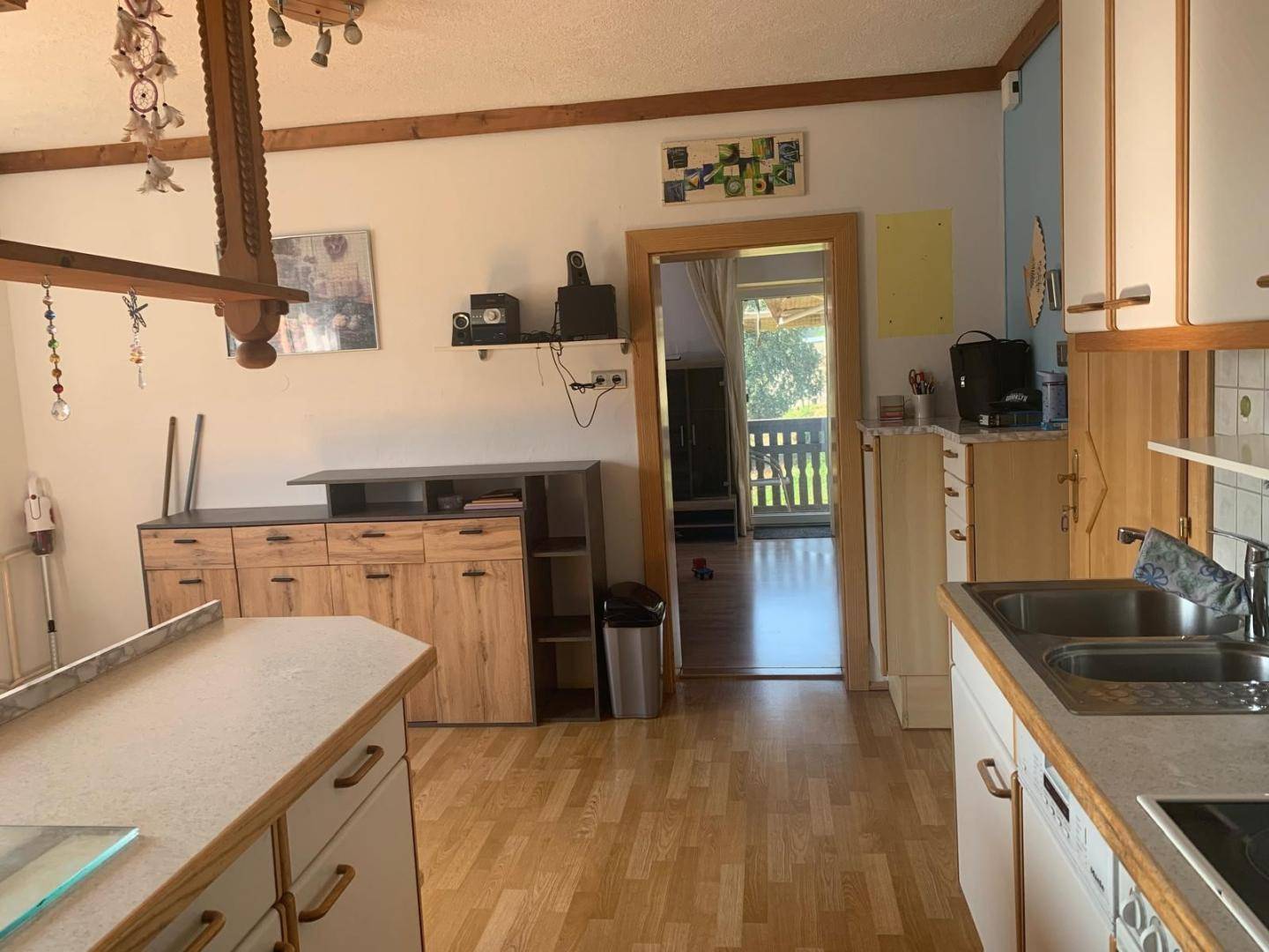 Geräumige Küche mit Holzschränken, Doppelspüle und Durchgang zu einem weiteren Wohnbereich.