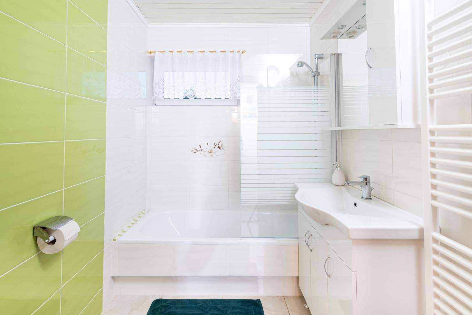 Modernes Badezimmer mit grünen Wandfliesen, Badewanne, Dusche und Handtuchheizkörper.