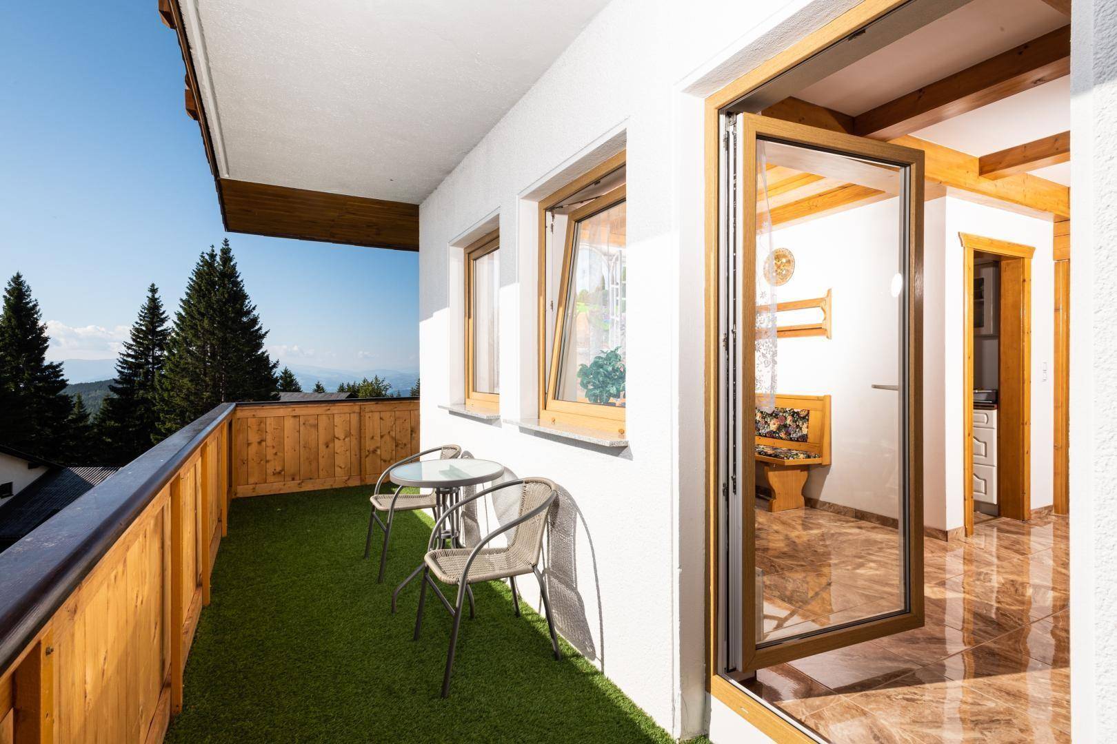 Balkon mit Kunstrasen, Sitzgelegenheiten und Zugang zum Innenbereich, umgeben von Natur.