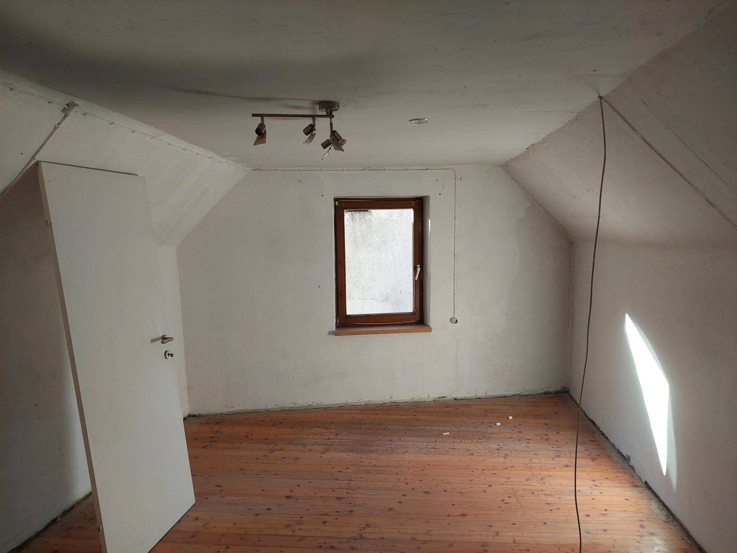 Dachgeschosszimmer mit schrägen Wänden, einem Fenster und Holzdielenboden, bereit zur Gestaltung.