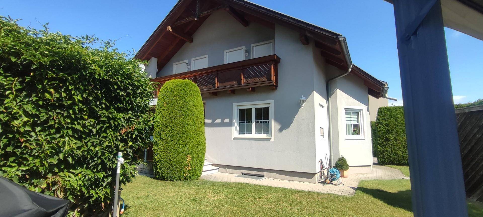 Seitenansicht des Hauses mit grünem Rasen, Hecke und einem kleinen Balkon im Obergeschoss.